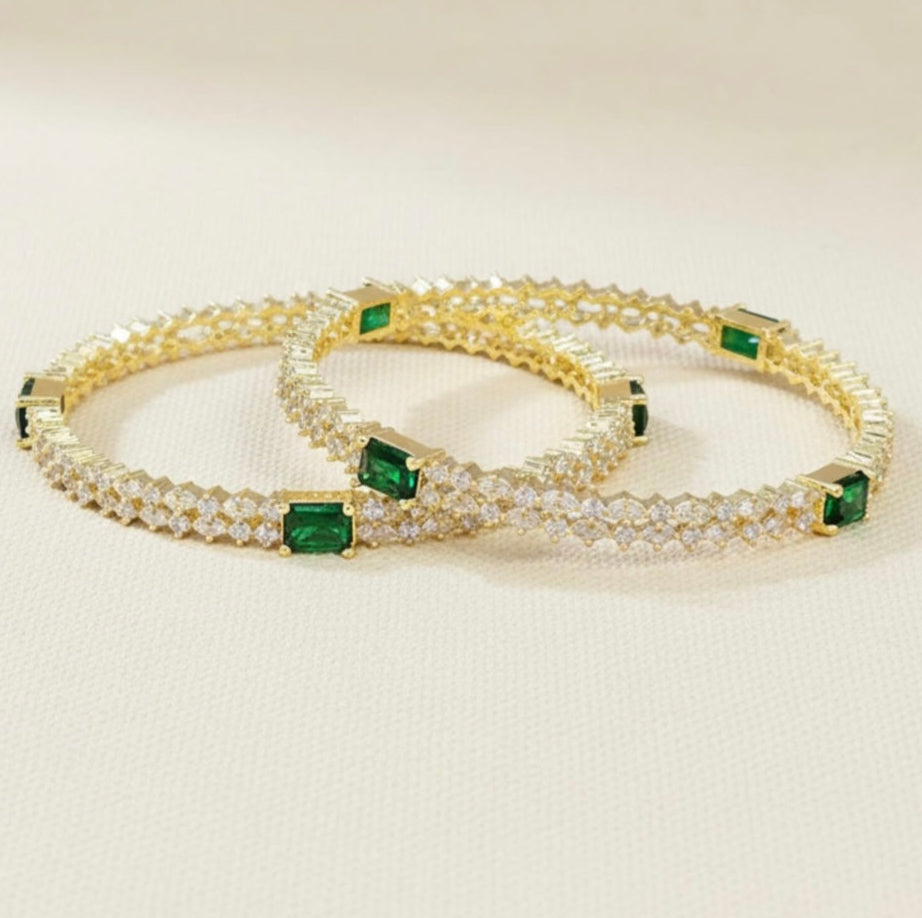 Two diamond and emerald bangles on a beige background